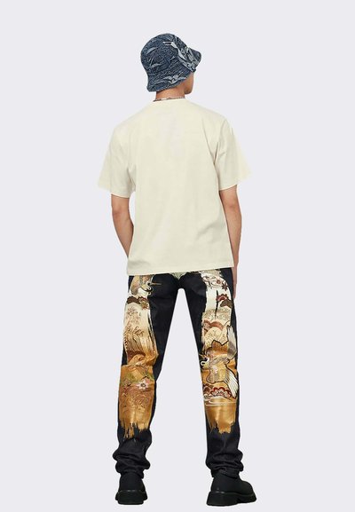 T-shirt color crema e jeans neri con motivi colorati e intricati. Il cappello a secchiello rotondo è in denim con un disegno floreale.