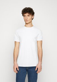 Hvitt bomull t-skjorte med korte ermer, rund hals, og en enkelt brystlomme, kombinert med blå denim jeans. Minimalistisk design.