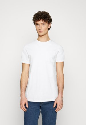 Hvid bomulds t-shirt med korte ærmer, rund halsudskæring og en enkelt brystlomme, parret med blå denim jeans. Minimalistisk design.