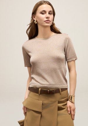 Korte mouwen, lichtbeige metallic breisel top met een ronde halslijn en een losse pasvorm, gecombineerd met kaki geplooide broeken en een bruine riem.