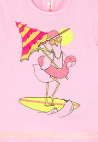 T-shirt rosa com um flamingo brilhante em uma prancha de surf, usando óculos de sol e um chapéu de sol, com um guarda-sol listrado e um design de sol.