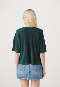 Grønn plissert topp med korte ermer, med rund hals, kombinert med et slitt denim mini-skjørt med baklommer.