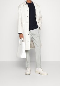 Biały płaszcz trencz, granatowy sweter, jasnoszare spodnie, beżowe buty i biały torba na ramię. Charakteryzuje się gładkimi tkaninami i minimalistycznym designem.