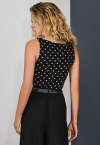 Black sleeveless top with white polka dots, paired with high-waisted black trousers featuring a black belt and side pockets.