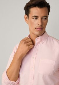 Camicia button-up rosa chiaro realizzata in tessuto morbido, dotata di una singola tasca sul petto e di un colletto classico con una vestibilità leggermente rilassata.