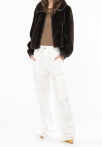 Brązowa kurtka z sztucznego futra, białe spodnie cargo z kieszeniami, beżowa bluzka oraz buty w neutralnych odcieniach. Strukturalny design z luźnym krojem i detalami.