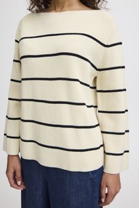 Kremfarget ribbestrikket genser med svarte horisontale striper, bred båtnekk, og lange ermer. Kombinert med blå denimbukser.