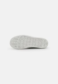 Semelle en caoutchouc blanche avec des motifs de grip circulaires et une texture grenu. Comprend un logo en relief et un marquage de taille sur le côté.