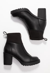 Schwarze Absatzstiefeletten aus einer Kombination von glattem Leder und strukturiertem Stoff, mit einem Reißverschluss und markanten strukturierten Gummisohlen.