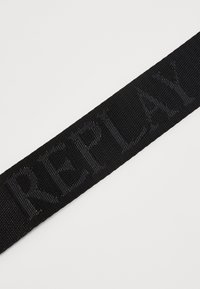 Sort vævet stofrem med prægede "REPLAY" bogstaver langs længden. Glat tekstur med et minimalistisk design.