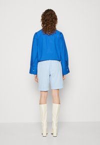 Camisa de manga larga azul combinada con pantalones cortos azul claro. Botas blancas hasta la rodilla completan el atuendo. Diseño sencillo y estilo casual.