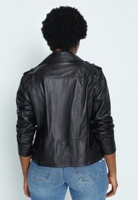 Zwarte leren motorjack met een gestructureerd ontwerp, schouderepauletten en textuurmouwen. Draag het over een blauwe spijkerbroek.