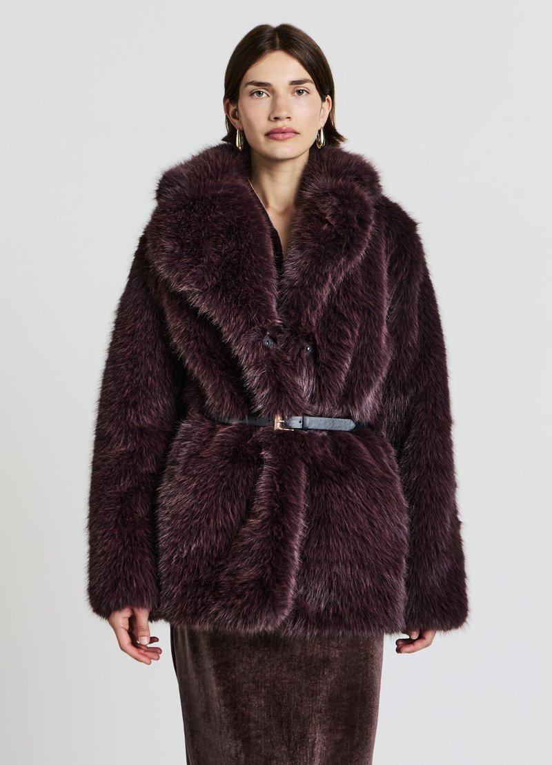 Giacca in pelliccia sintetica viola profondo e morbida con ampio colletto, vita con cintura e due bottoni frontali. Superficie testurizzata e soffice con un aspetto lussuoso.