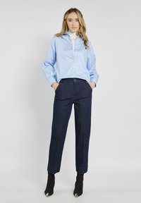 Jasnoniebieska koszula z długim rękawem, zestawiona z ciemnoniebieskimi spodniami dżinsowymi. Czarne botki za kostkę z wydłużonym noskiem dopełniają stylizację.