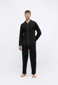 Conjunto de pijama negro hecho de una tela suave, que cuenta con mangas largas, una blusa con botones y un ribete blanco en contraste, y pantalones holgados a juego.