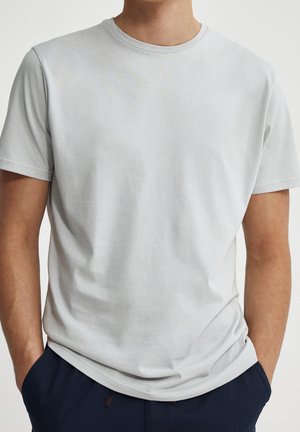 T-shirt en coton gris clair avec un col rond, des manches courtes et une coupe décontractée. Texture lisse, design minimal, sans motifs ni accents visibles.