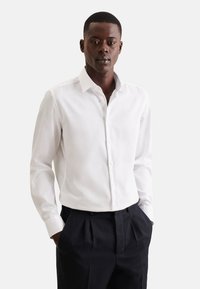 Witte blouse met lange mouwen en knopen, gemaakt van een gladde stof, met een klassieke kraag en een getailleerd ontwerp, gecombineerd met donkere, op maat gemaakte broeken.