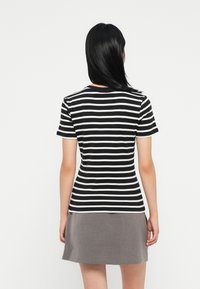 Svart-hvit stripete t-skjorte med korte ermer, rund hals og en tettsittende design. Kombinert med et grått skjørt, som skaper et lagdelt utseende.