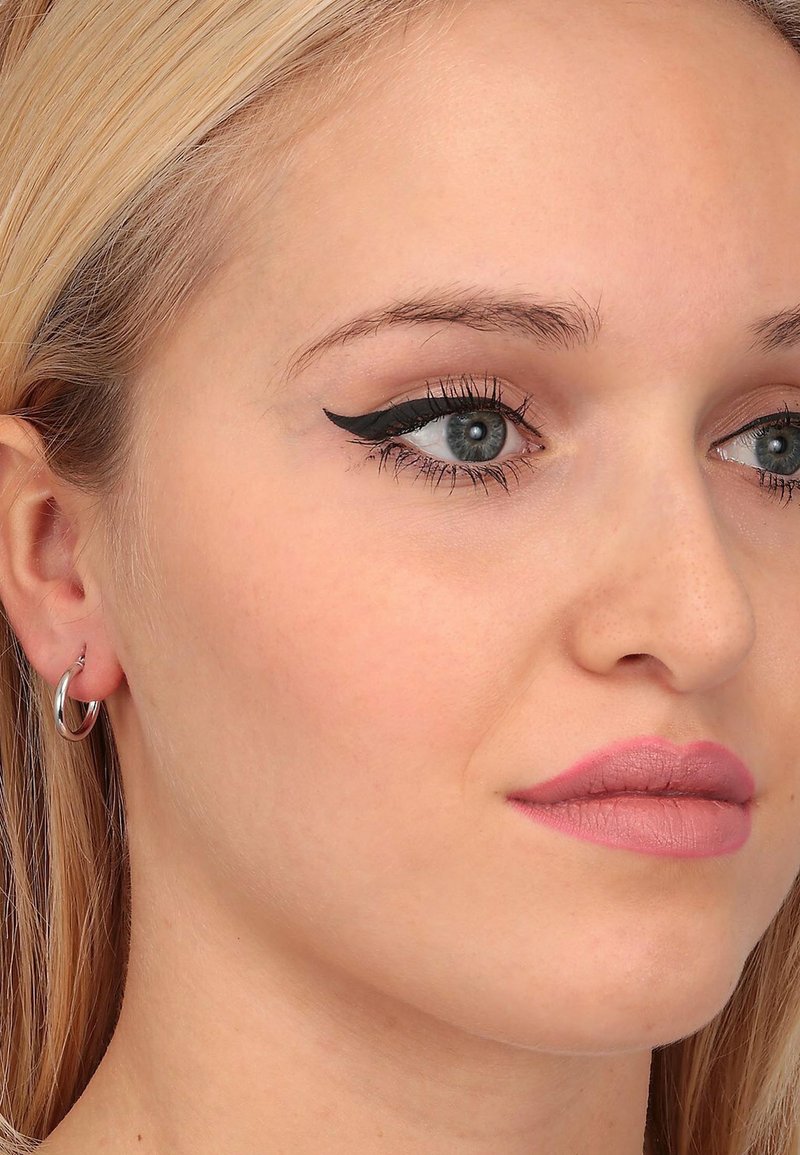 Primo piano di un volto con pelle liscia, capelli biondo chiaro, orecchino a cerchio argento, eyeliner a ala e rossetto rosa chiaro. Sfondo neutro.