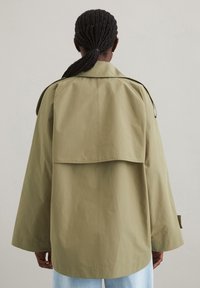 Overdimensioneret khaki jakke med en afslappet pasform, der har en rygklap, brede ærmer og en mat tekstur. Minimal hardware og neutral farve.