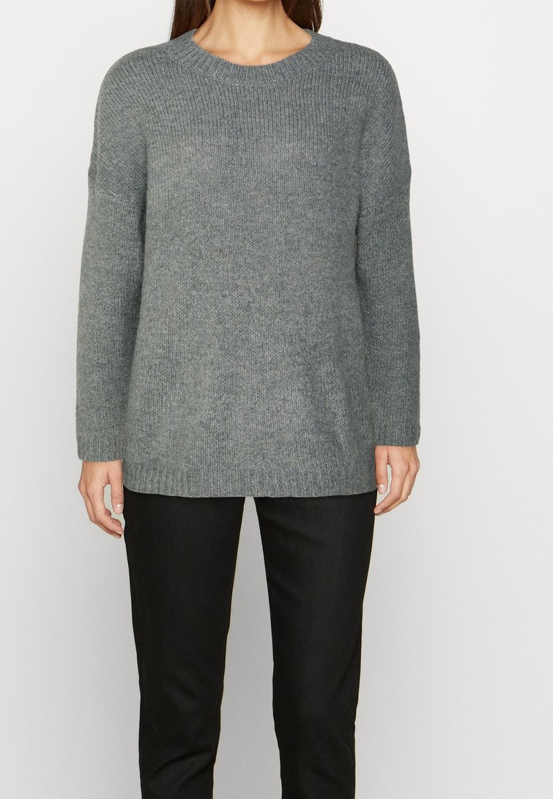 Szary sweter z dzianiny z okrągłym dekoltem i długimi rękawami. Posiada prążkowany dół i mankiety. W zestawie z ciemnymi spodniami.