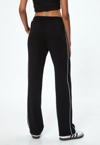 Zwarte sweatpants met een relaxte pasvorm, voorzien van witte zijkanten, een elastische tailleband en een zachte textuur.