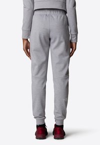 Grijze sweatpants met een elastische tailleband, taps toelopende pijpen, en een logo-details bij de enkel. Draagt met donkerrode sportschoenen.