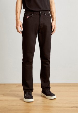 Zwarte denim jeans met een getailleerd ontwerp, met een klein geborduurd logo op de voorzak. Gecombineerd met zwarte sneakers.