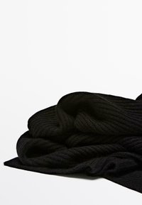 Svart stickad halsduk med en ribbad textur, tillverkad av mjukt, tjockt tyg. Halsduken hängs löst, vilket framhäver dess flexibilitet och värme.