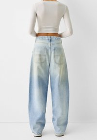 Light blue high-waisted jeans with a wide-leg fit, featuring two back pockets and subtle fading. Cotton fabric with a soft texture.