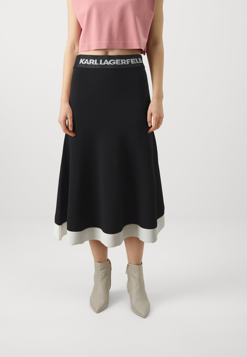 Svart skjørt med ribbet hvit kant og grå elastisk midjebånd med "KARL LAGERFELD" branding; paret med spisse beige ankelstøvler.