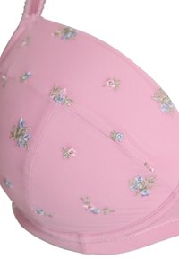 Sujeción de sujetador rosa con pequeños patrones bordados de flores azules y rosas y una tira visible sobre un fondo blanco.