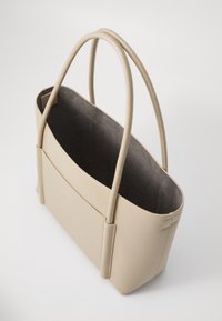 Borsa tote in pelle beige con due manici lunghi e una superficie liscia. Interno in suede grigio con tasca a scomparsa. Apertura superiore arrotondata.