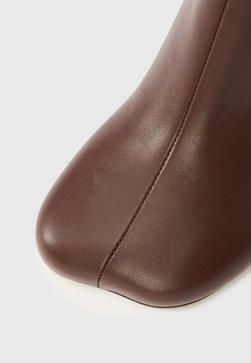 Brown leather ankle boot with a pointed toe, smooth texture, and visible stitching detail along the seam.