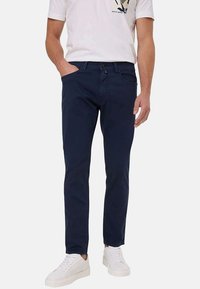 Chinos bleu marine en coton à coupe slim, avec poches avant, fermeture à bouton, associés à des baskets blanches.