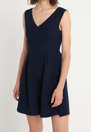 Mørkeblå ærmeløs kjole med V-hals, tætsiddende bodice og vidde skørt. Lavet af glat stof med sidelæg for ekstra detaljer.