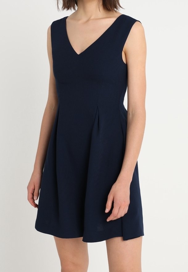 Námořnicko-modré šaty bez rukávů s výstřihem do V, přiléhavým korzetem a rozšířenou sukní. Zhotovené z hladké tkaniny, s bočními sklady pro přidaný detail.