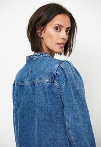 Denim jacket met een blauwe kleur, gestructureerde kraag, pofmouwen en een geborduurd logo op de rug. Soepele textuur en klassiek ontwerp.
