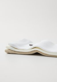 Tres pares de calcetines apilados: uno blanco con textura de tricot, uno crema y uno beige con borde acanalado y acentos en contraste.