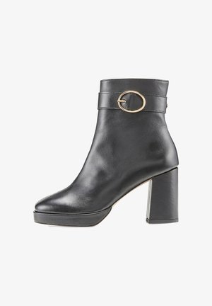 Bottine en cuir noir avec un talon épais, bout rond et accent circulaire en or sur la sangle. Texture lisse et design minimaliste.