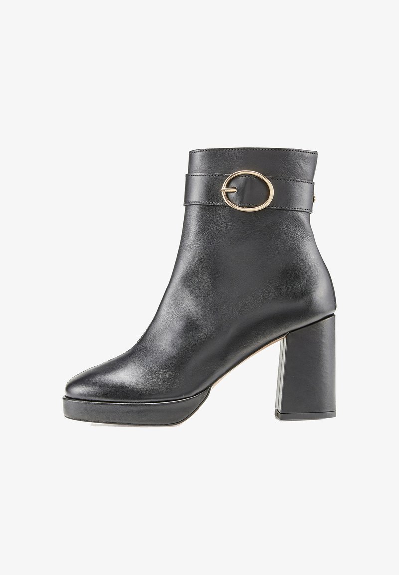 Bottine en cuir noir avec un talon épais, bout rond et accent circulaire en or sur la sangle. Texture lisse et design minimaliste.