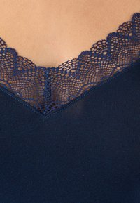 Canottiera blu navy con scollo a V. Presenta un bordo in pizzo ondulato all'collo e una morbida texture a coste.