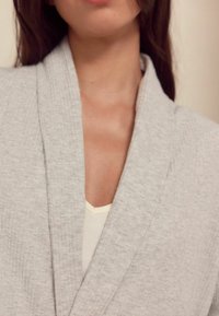 Lichtgrijze, geribde cardigan met een sjawl kraag, over een crèmekleurig, aansluitend topje, dat een zachte textuur en een ontspannen ontwerp tentoonstelt.