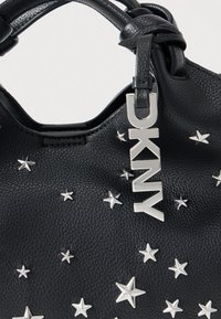 Sac à main en cuir noir avec des décorations en forme d'étoiles argentées et une étiquette logo DKNY argentée. Texture lisse avec un design structuré.