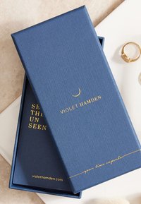 Kobaltblauwe gestructureerde geschenkdoos met gouden opdruk, met de tekst "VIOLET HAMDEN" en een citaat. Inclusief een donkere binnenvoering met aanvullende tekst.