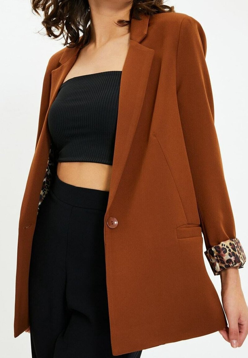 Blazer marrón con un diseño estructurado, cierre de un solo botón y detalles de estampado de leopardo en las mangas. Tejido suave, corte ajustado y mangas largas.