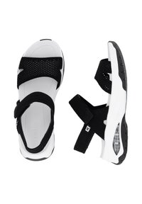 Sandales noir et blanc avec un dessus en mesh, des straps réglables et une semelle texturée avec une unité d'air visible. Conçues pour le confort et le soutien.