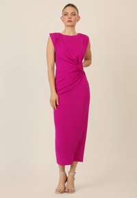 Vestido midi fucsia con detalle fruncido en la cintura, diseño sin mangas y tela suave. Llevado con tacones plateados con tiras.