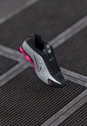 Czarny i srebrny but do biegania marki Nike z różowymi akcentami, spoczywający na teksturowanej metalowej siatce.