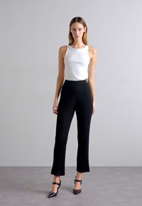 Black ribbed knit pants with a flared hem, paired with a fitted white tank top and pointed black heels, on a neutral background.